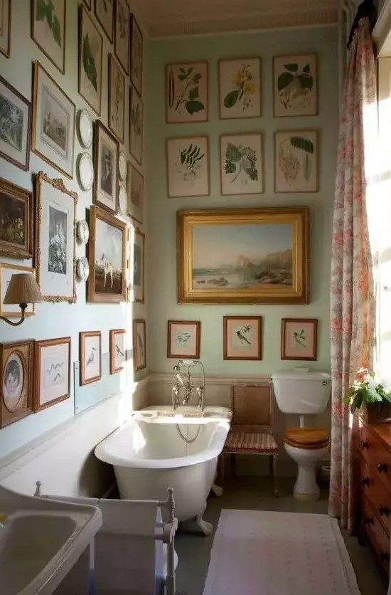 a vintage bathroom with light green walls, a gallery wall that covers two walls at once, a clawfoot bathtub and a free-standing sink