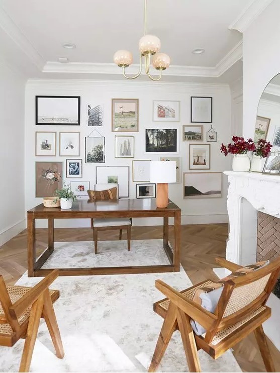 a vintage home office with a stained desk and chairs, an elegant fireplace, a large gallery wall and an arched mirror