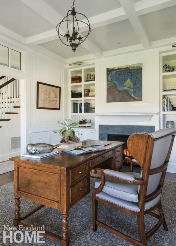 a vintage home office with built-in bookshelves, a fireplace, a dark-stained desk and a grey chair, a sphere pendant lamp
