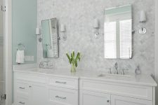 a vintage neutral bathroom with a mint green accent wall, a white marble arabesque tile wall, white vanities and sconces and mirrors