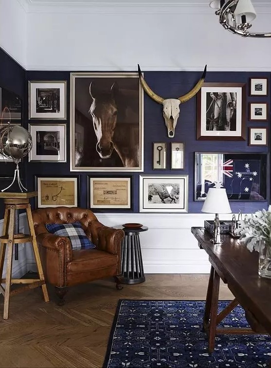 a vintage rustic home office with a stained desk, a leather chair, a large gallery wall on a cobalt wall and white paneling