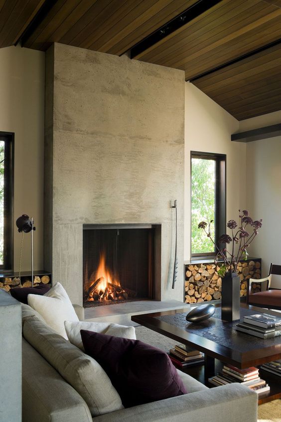 a welcoming living room with a stained wood ceiling, a concrete fireplace, neutral seating furniture, a coffee table and firewood storage