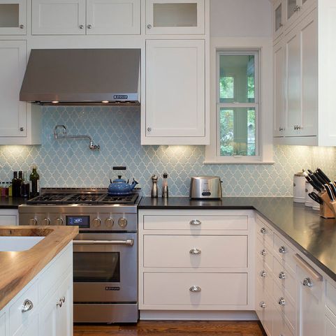 a white kitchen with black countertops, a light blue arabesque tile backsplash, stainless steel appliances and knobs