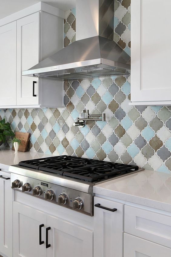 a white kitchen with shaker style cabinets, white stone countertops, a colorful arabesque tile backsplash and stainless steel appliances