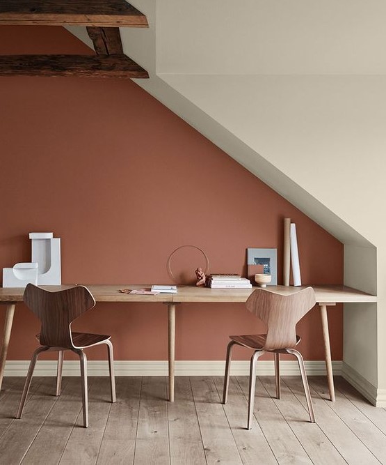 an attic shared work space with a shared desk, plywood chairs and a bold terracotta accent wall plus wooden beams