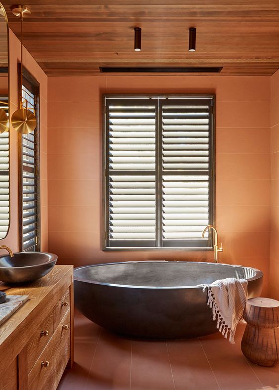 an earthy tone bathroom with burnt orange tiles and terracotta on the floor, a stained vanity, sinks and an oval tub