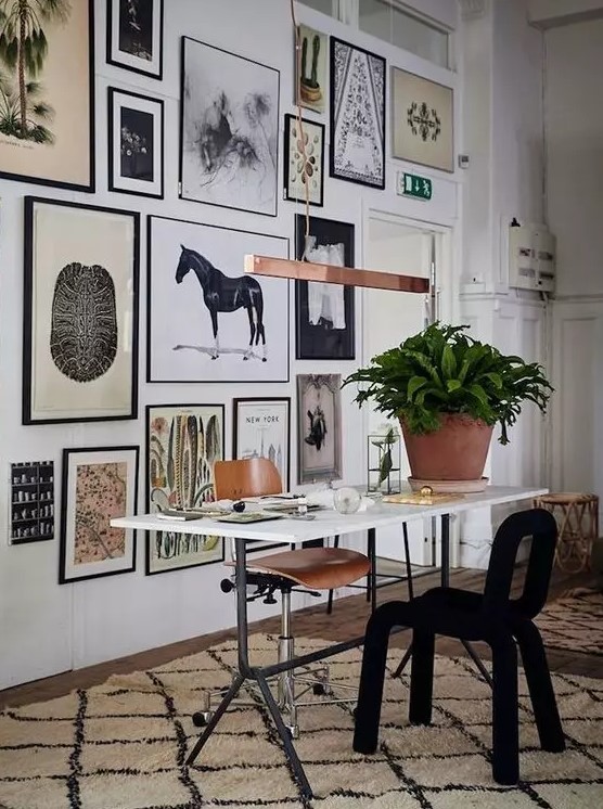 an eclectic home office with a lightweight desk, a plywood and black soft chair, an oversized gallery wall with potted plants
