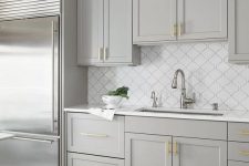 an elegant dove grey kitchen with shaker cabinets, gold handles, a white arabesque tile backsplash and gold and chrome touches