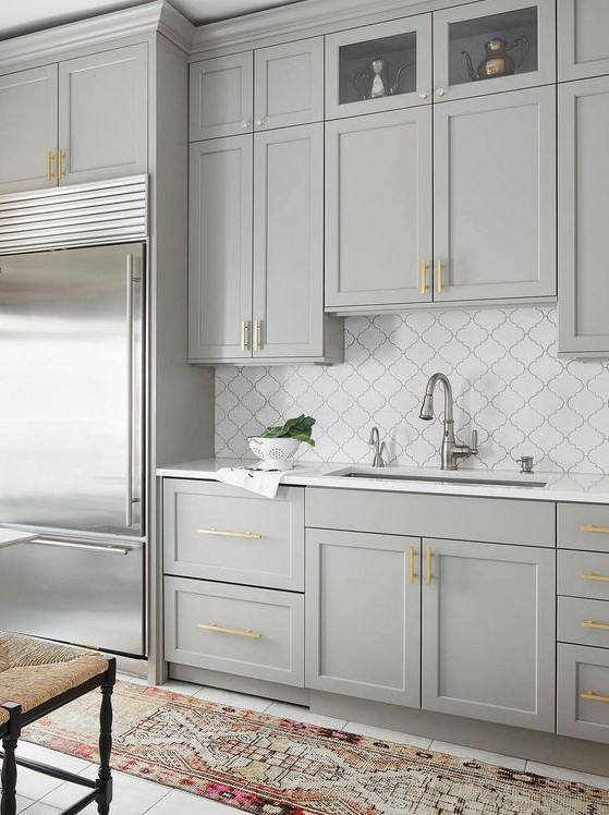 an elegant dove grey kitchen with shaker cabinets, gold handles, a white arabesque tile backsplash and gold and chrome touches