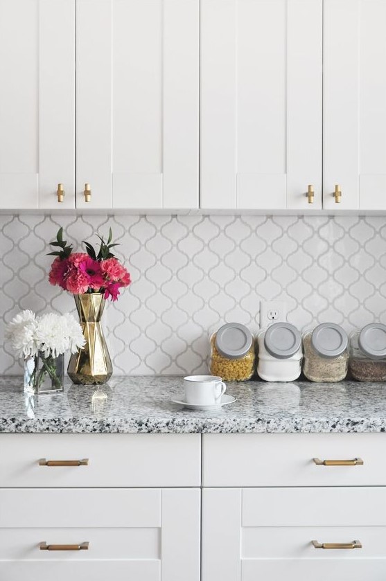 an elegant white kitchen with shaker cabinets and gold fixtures, a small scale arabesque tile backsplash and terrazzo countertops is very cool