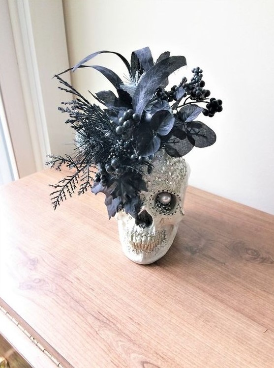 a Gothic Halloween decoration of an embellished skull with sequins and a pearl plus faux black blooms and leaves