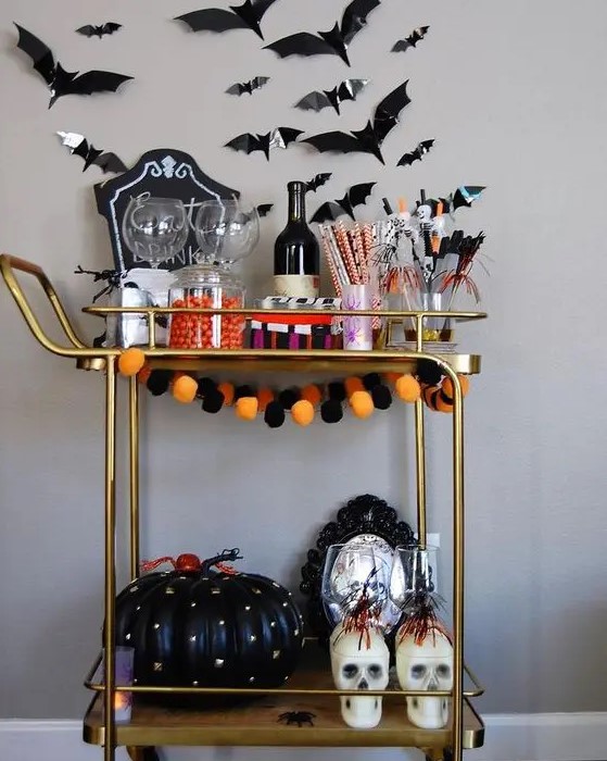 a bold Halloween bar cart with a bright pompom garland, a black spiked pumpkin, skulls, bats on the wall