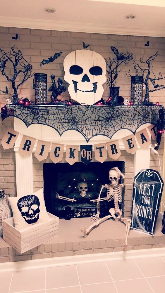 a chic Halloween fireplace with black spiderwebs, branches, bats, candles, a skeleton, a plaque skull and a banner