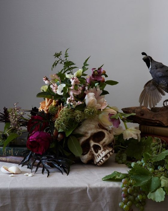 a moody Halloween centerpiece of a skull plus some blush and purple blooms and greenery and herbs