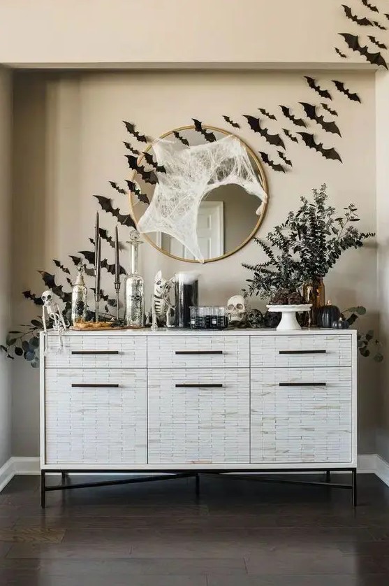 a cool console table with black bats, greenery in vases, skulls and skeletons, spiderwebs is a gorgeous idea for Halloween