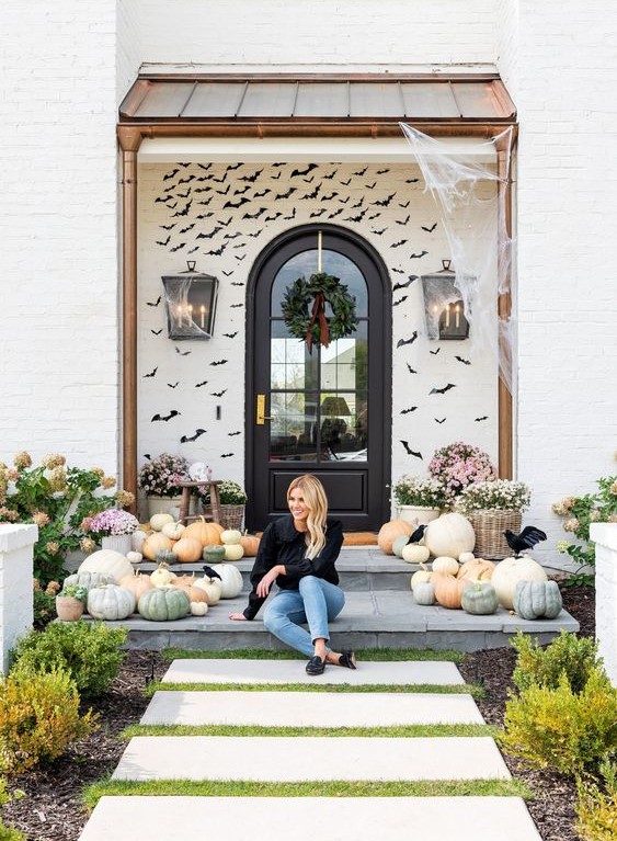 a farmhouse front porch done with lots of heirloom pumpkins, blooms in baskets and black paper bats covering the wall is amazing