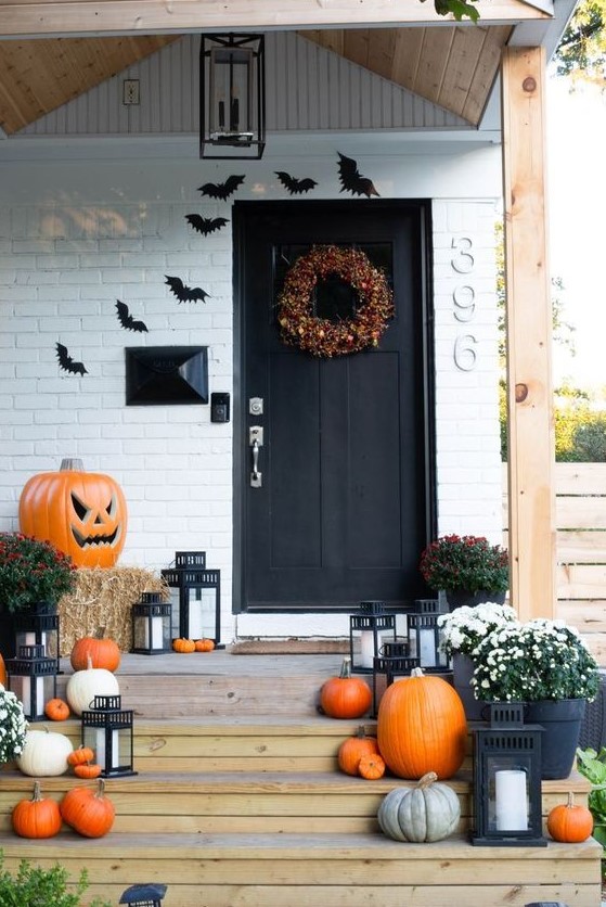 a farmhouse Halloween porch with natural pumpkins, hay, blooms and candle lanterns, black paper bats on the wall
