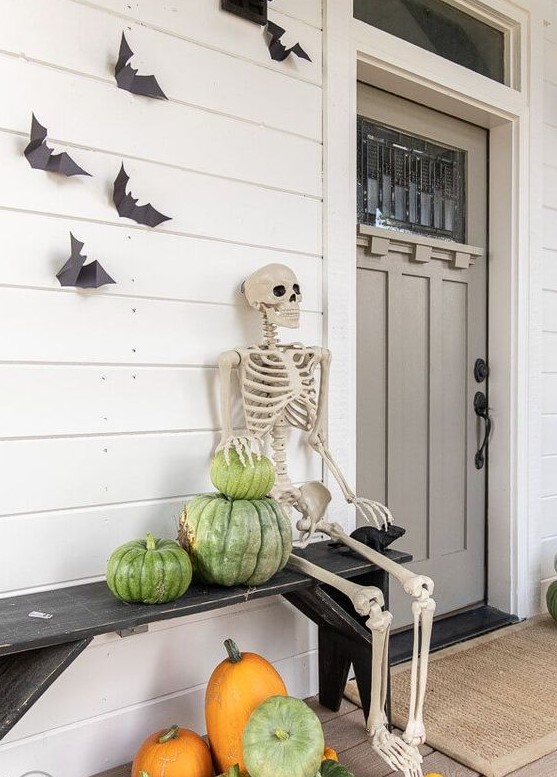 a rustic Halloween porch with heirloom pumpkins, a skeleton and some bats on the wall is a cool idea