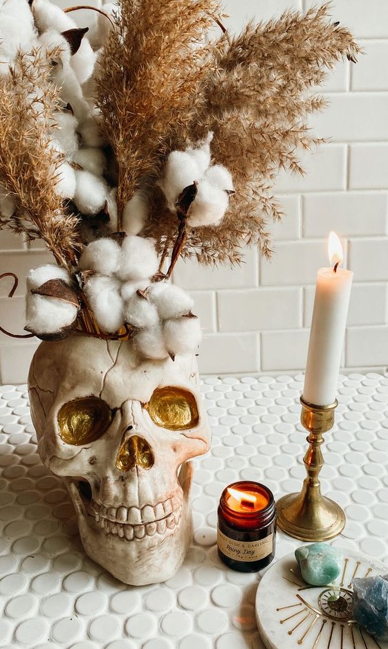 delicate Halloween decor with a neutral and gold skull vase, cotton branches, grasses and candles is a gorgeous idea