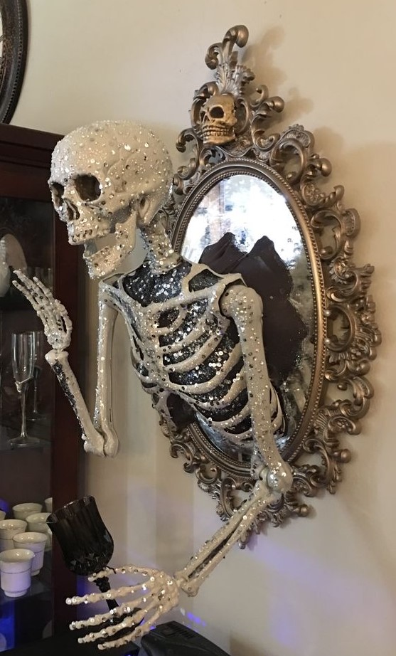 a scary glam Halloween decoration of a vintage mirror with a glam embellished half skeleton attached is elegant