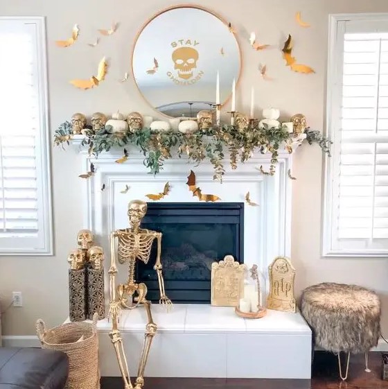 a white and gold Halloween fireplace with greenery, skulls, a skeleton, candles and bats