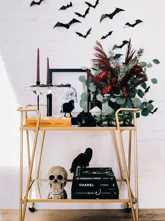 a Halloween bar cart with an embellished skull, a dark floral arrangement, burgundy candles and bats over the cart