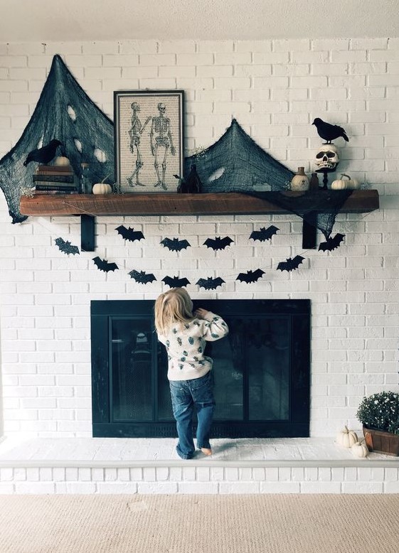 a Halloween mantel decorated with black paper bat buntings, black spider web and pumpkins plus skulls