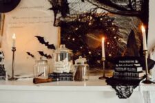 15 a Halloween mantel styled with black bats, a black wreath with lights, stacks of books, black branches and a black witch hat