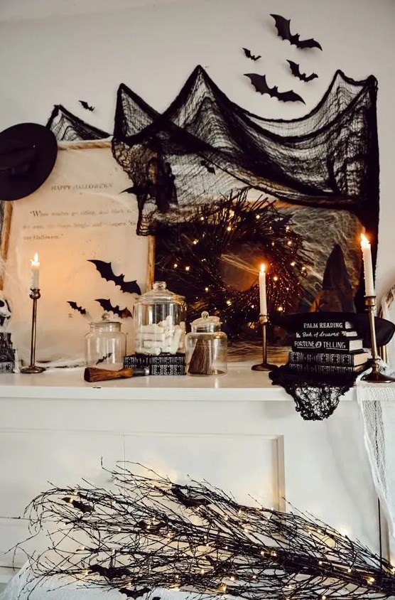 a Halloween mantel styled with black bats, a black wreath with lights, stacks of books, black branches and a black witch hat