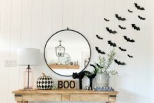 16 a modern farmhouse space with black paper bats attached to the wall, a wooden console with a black cat, BOO, a black and white printed pumpkin