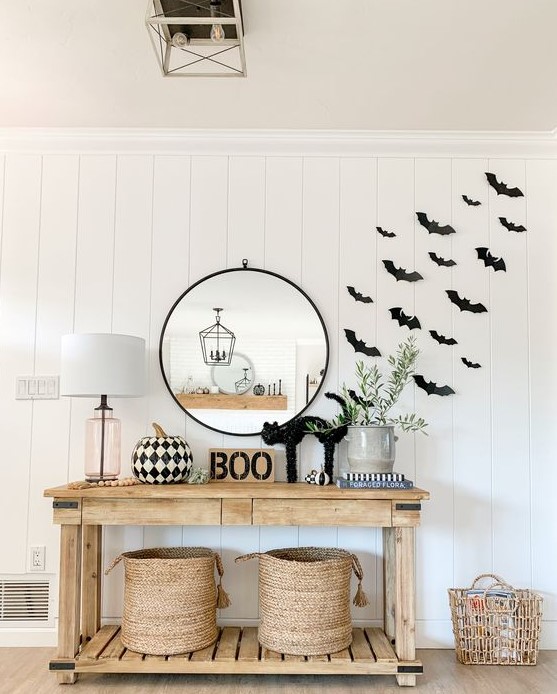 a modern farmhouse space with black paper bats attached to the wall, a wooden console with a black cat, BOO, a black and white printed pumpkin