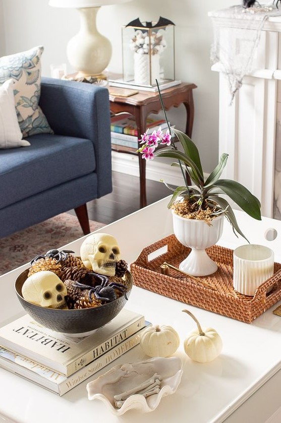 a chic Halloween coffee table with a potted bloom, a bowl with spiders, skulls and pinecones and some bones in a shell
