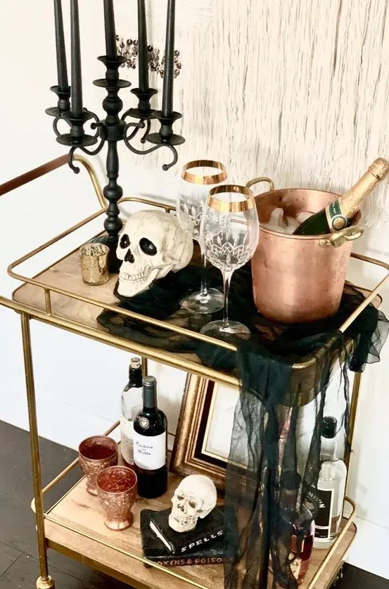 a Halloween bar cart with skulls, a black candelabra with black candles, black cheesecloth, copper barware and elegant glasses