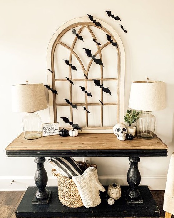 a stylish rustic vintage console table with black and white pumpkins, a skull, a vintage window frame and black paper bats covering it