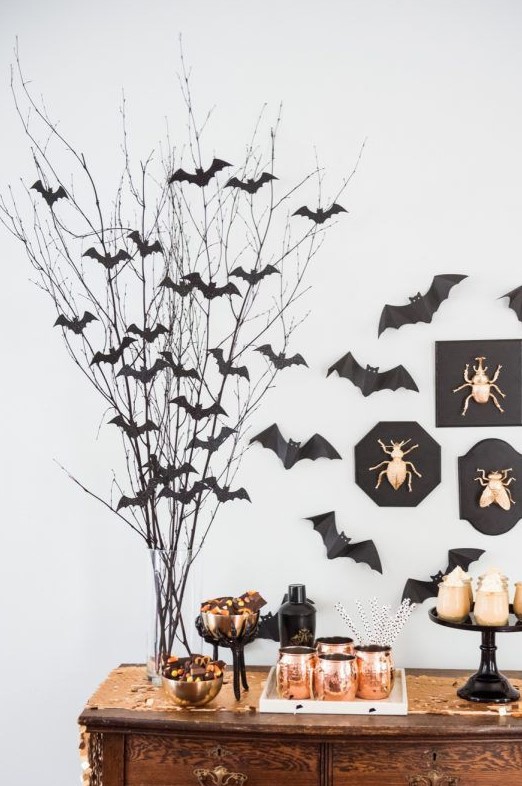 a sweets table with branches with black paper bats attached to them and to the wall, gilded bugs in frames