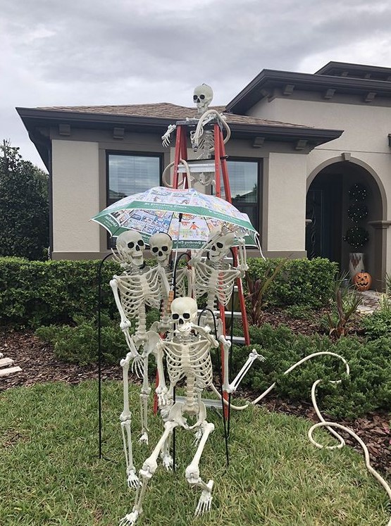 a fun skeleton scene sitting on a ladder and with an umbrella is a cool idea for Halloween outdoor styling