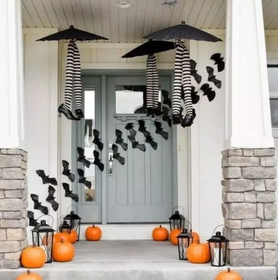 a whimsy Halloween porch with witches' legs and umbrellas, orange pumpkins, candle lanterns and bats