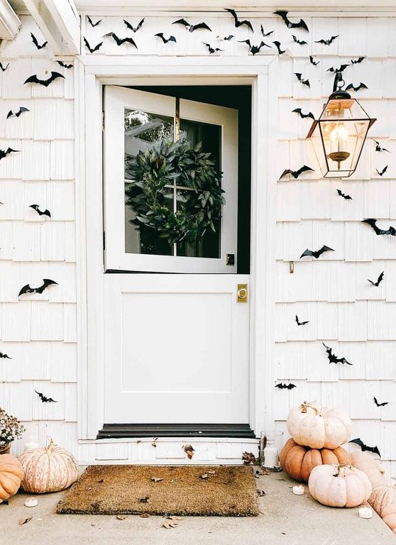 a white farmhouse with black paper bats covering the walls, heirloom pumpkins stached and some fall leaves is awesome