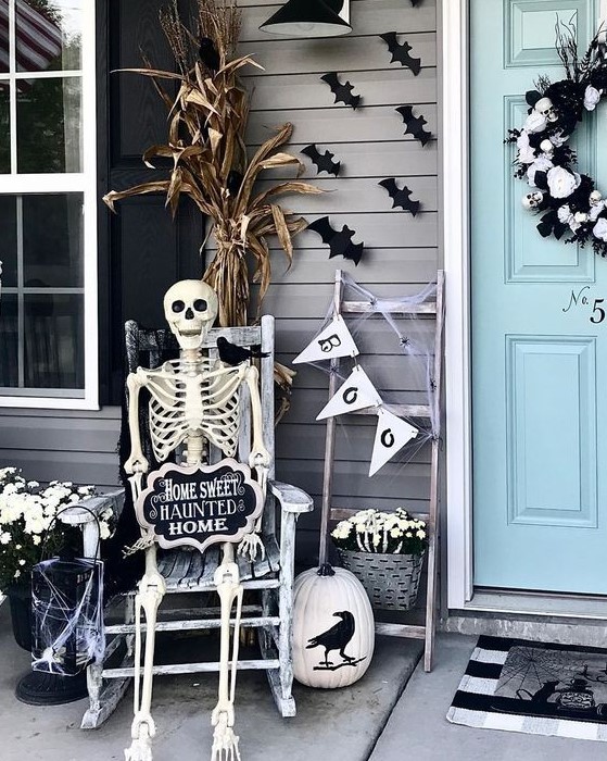 a Halloween porch with bats, a bunting, a skeleton rocking, cron husks and a skull wreath on the door is a cool idea