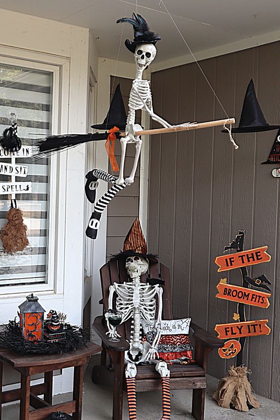 a Halloween porch with skeletons sitting on the lounger and broom, with witches' hats, signs and lanterns