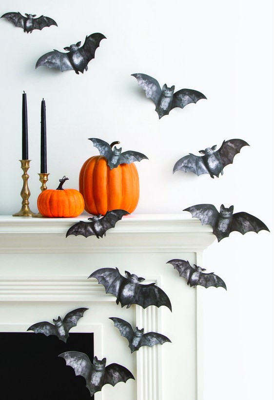 beautiful painted black paper bats attached to the wall and mantel, orange pumpkins and black candles in gold candlesticks