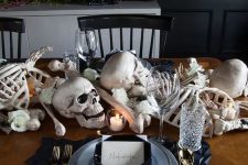 33 a stylish Halloween tablescape with bones, skulls, candles, white blooms, black geometric placemats and plates, gold cutlery