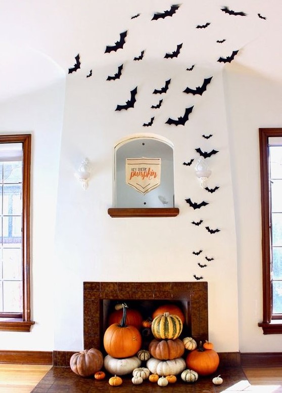 modern Halloween decor with a fireplace filled with pumpkins and black paper bats is a lovely idea for the flal