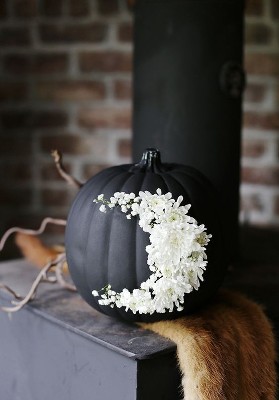 a matte black pumpkin decorated with white blooms is a very sophisticated and chic idea for Halloween