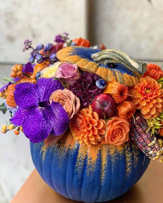 a stunning Thanksgiving pumpkin in electric blue with yellow, with orange, violet, deep purple and burgundy blooms, corn cobs and apples
