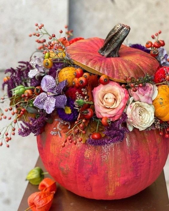 a super colorful fall pumpkin decirated with white, purple and pink blooms, berries and fruits and greenery is amazing