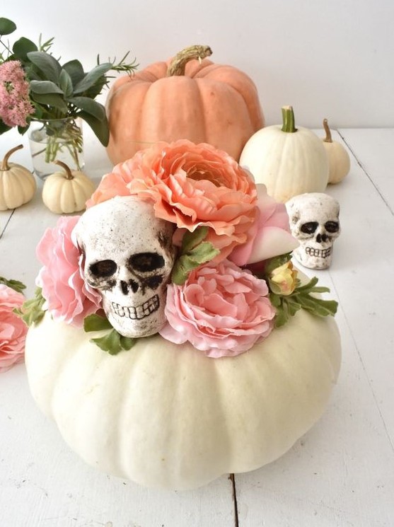 pretty Halloween decor of a white pumpkin, pink faux blooms and skulls is a lovely idea for a pastel Halloween party