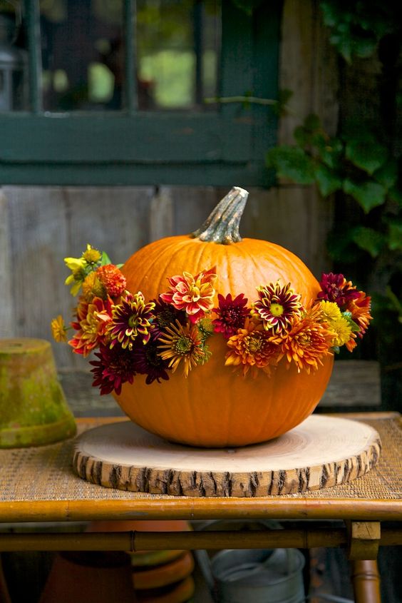 an orange pumpkin decorated with seasonal blooms in orange, burgundy and yellow is amazing for fall decor