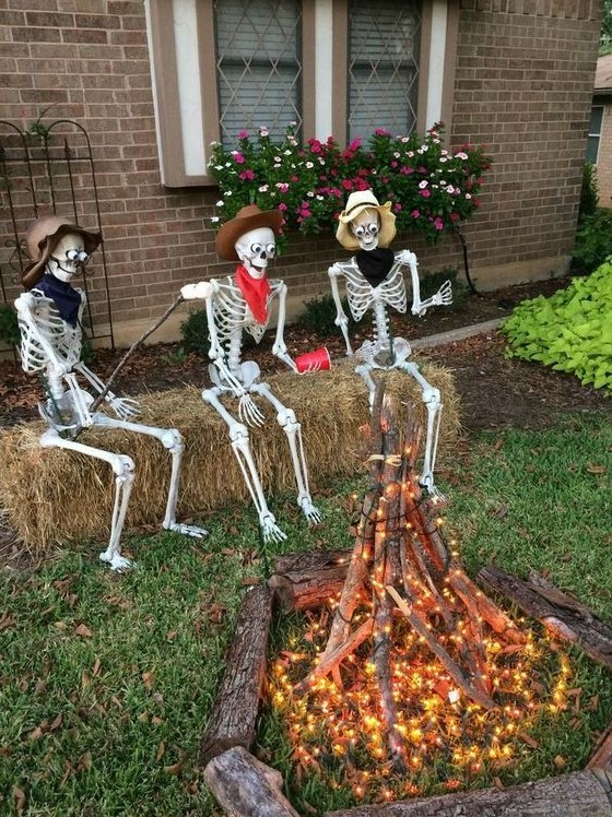 an outdoor Halloween scene with skeletons sitting around the fire made of branches and lights is a cool idea for your outdoor space