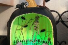 a black and green inside pumpkin wiht a graveyard, a fence, a skeleton, bats and branches is a gorgeous idea of a diorama